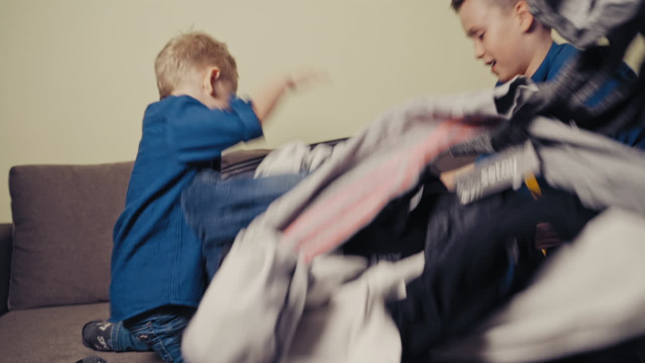 Cheerful boys and a valise with different clothes on the couch in the room. Two happy brothers taking the things out of a suitcase at home.
