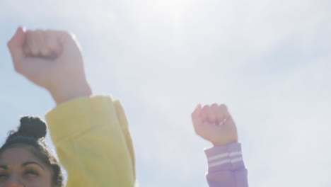 diverse group of female friends raising fists at the beach