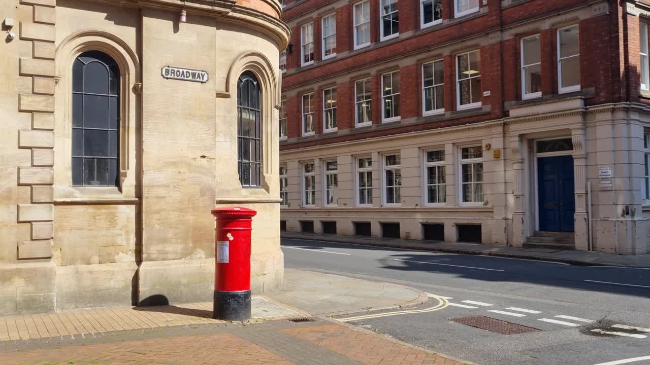 Revealing shot of historic Broadway in central Nottingham, England, featuring classic architecture and a bright red letterbox under a sunny summer sky