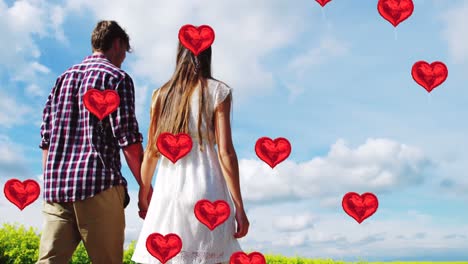 Multiple-heart-balloons-floating-against-man-and-woman-holding-hands-and-walking