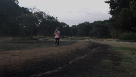 Early-in-the-morning,-a-woman-begins-to-jog-or-run-in-the-park-surrounded-by-trees-as-the-sun-rises-behind-the-tree