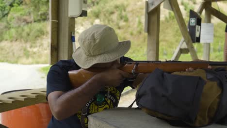 retrato de un hombre concentrado con sombrero de cubo apuntando con un rifle de madera al campo de tiro
