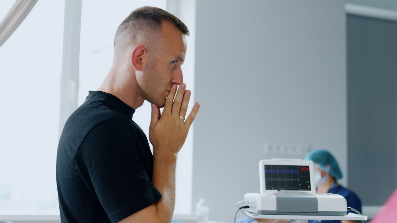 Caucasian man standing his hands folded in front of his face. Husband worries for his wife delivering a baby.