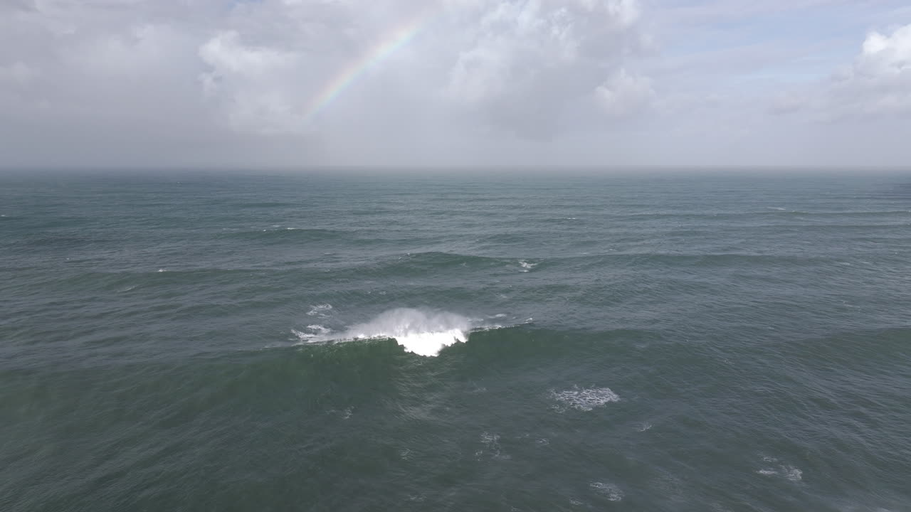 Aerial drone shot of big Atlantic Ocean waves coming into shore on a day with giant waves in Nazaré, Portugal, Europe. Drone flying towards rainbow and waves