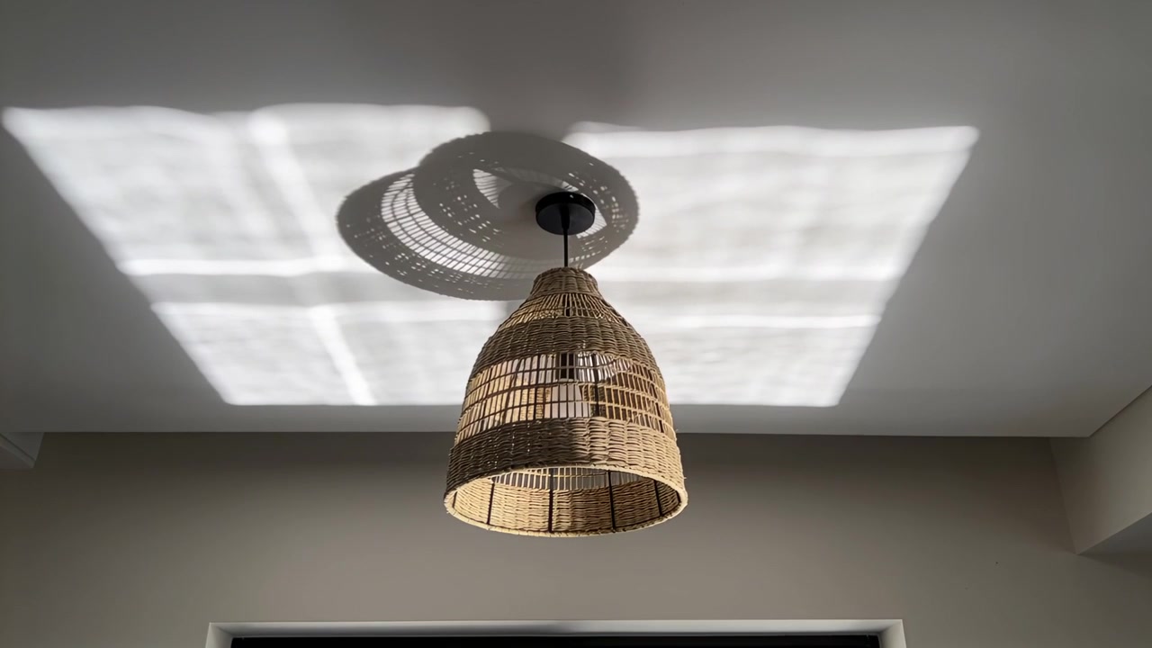 Sich bewegender Rattan-Sonnenschutz wirft gewebten Schatten über die Zimmerdecke, Sonnenlicht fällt durchs Fenster.