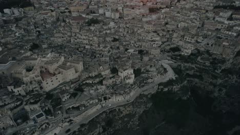 drone flying backwards with the camera tilting up slowly filming the old white city of matera at sunset in 4k