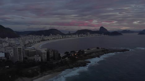 panorámica lateral aérea temprano en la mañana que muestra el amanecer sobre la playa de copacabana con el fuerte de copacabana en primer plano y el pan de azúcar en el fondo