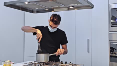 young man is cooking food for delivery in his restaurant in protective mask