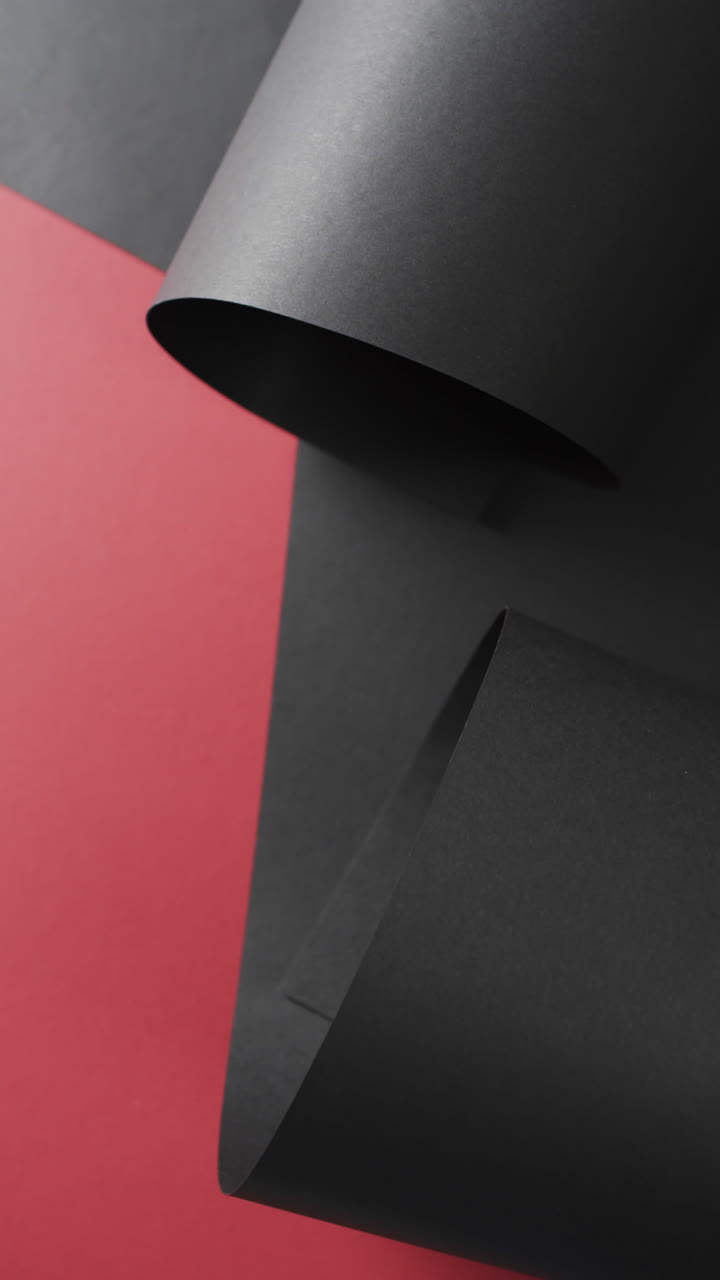 Vertical video of close up of rolled up black paper and copy space on red background