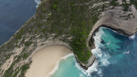 top view of steep cliffs at kelingking beach with waves crushing ashore, nusa penida, bali, indonesia. aerial shot