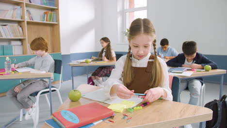 multiethnic group of kids in classroom writing in their notebook and smiling during english class at school