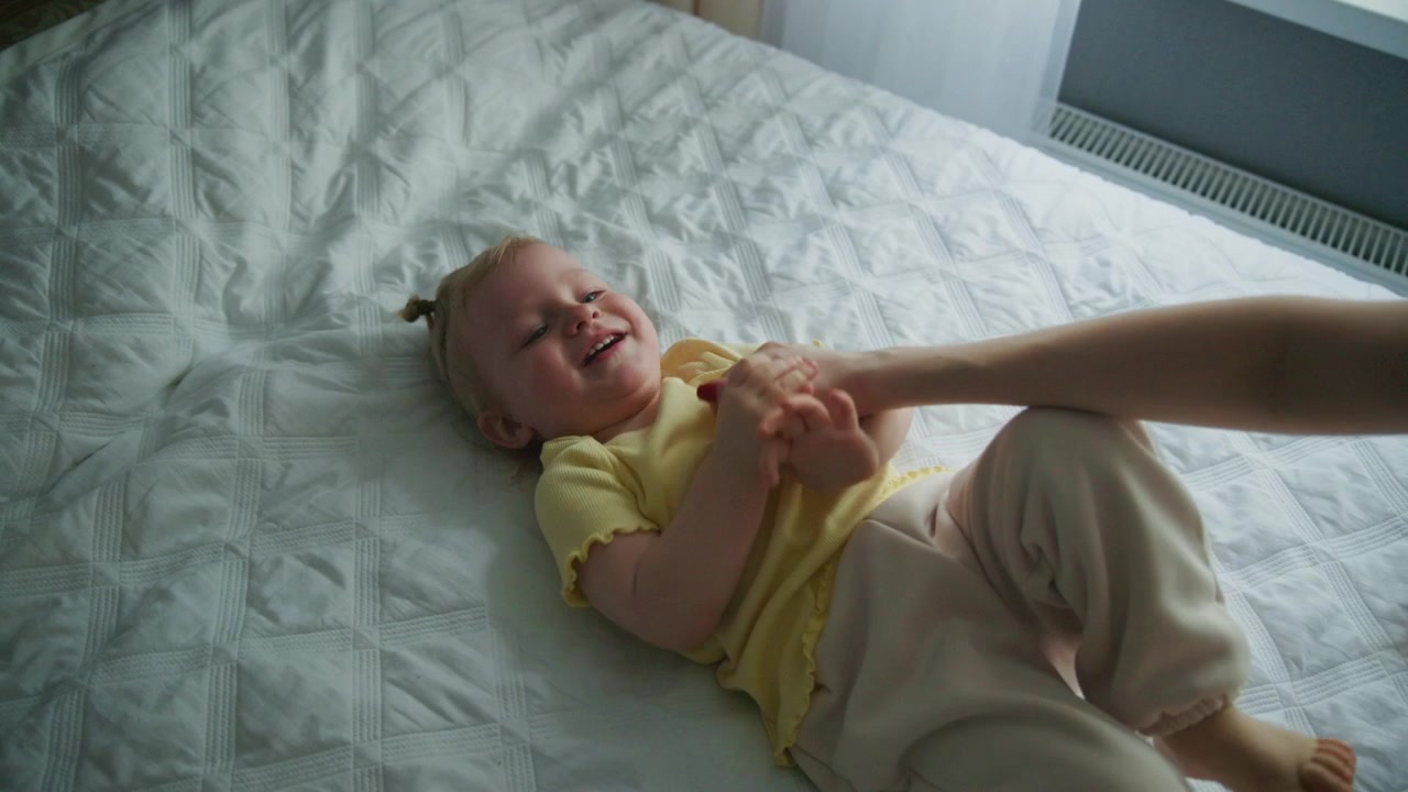 Mother Playing and Holding Hands with Toddler Daughter on Bed