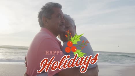 Animation-of-happy-holidays-text-over-happy-senior-biracial-couple-embracing-on-beach-at-christmas