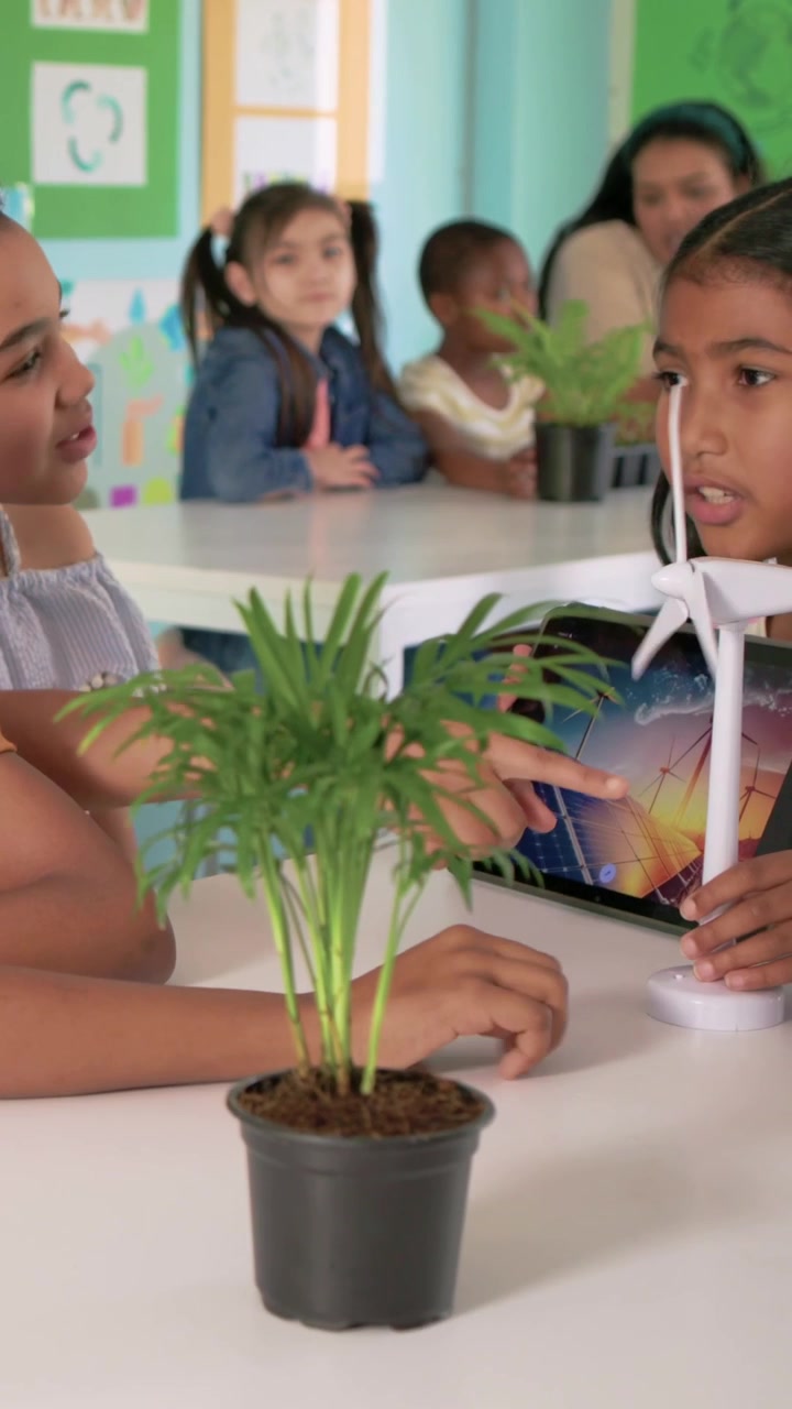 Vertical video: Reaching turbine, right kid adjusting blade, using tablet for STEM class with plant