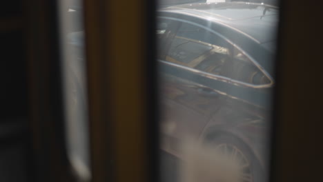 view through moving vehicle window shows car tail rolling along sunlit winter road, soft blur from foggy glass and frames, subtle motion of urban traffic, exhaust haze drifting, reflective asphalt