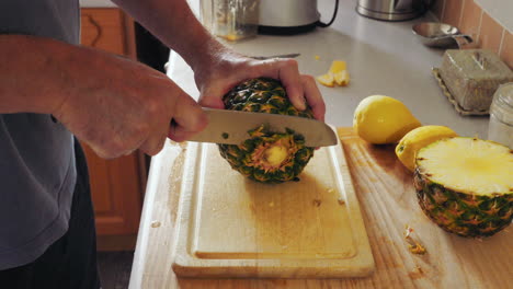 cutting the rough skin off a pineapple, footage shows hands of a man with knife slicing through the skin