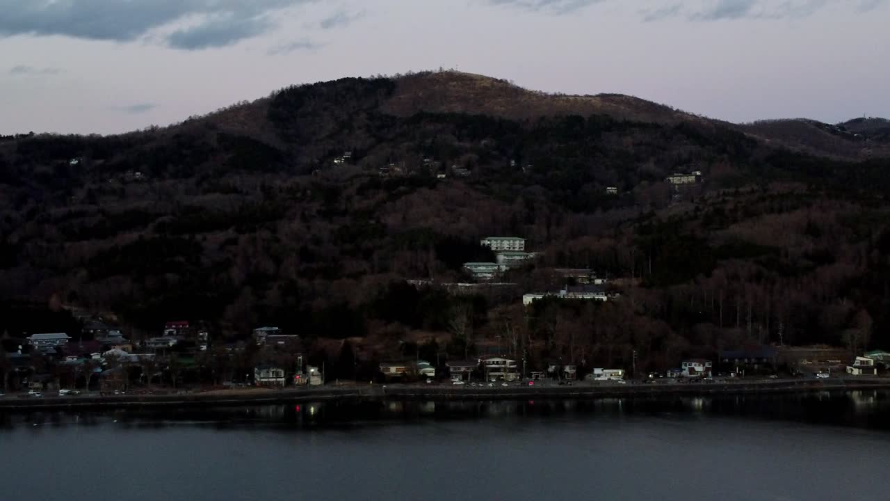 el crepúsculo desciende sobre una serena ciudad a orillas del lago con colinas boscosas y un claro reflejo en el agua, filmado con poca luz