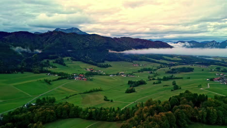 aerial drone forward moving shot over green farmlands surrounded by mountain range on all sides in norway on a cloudy day