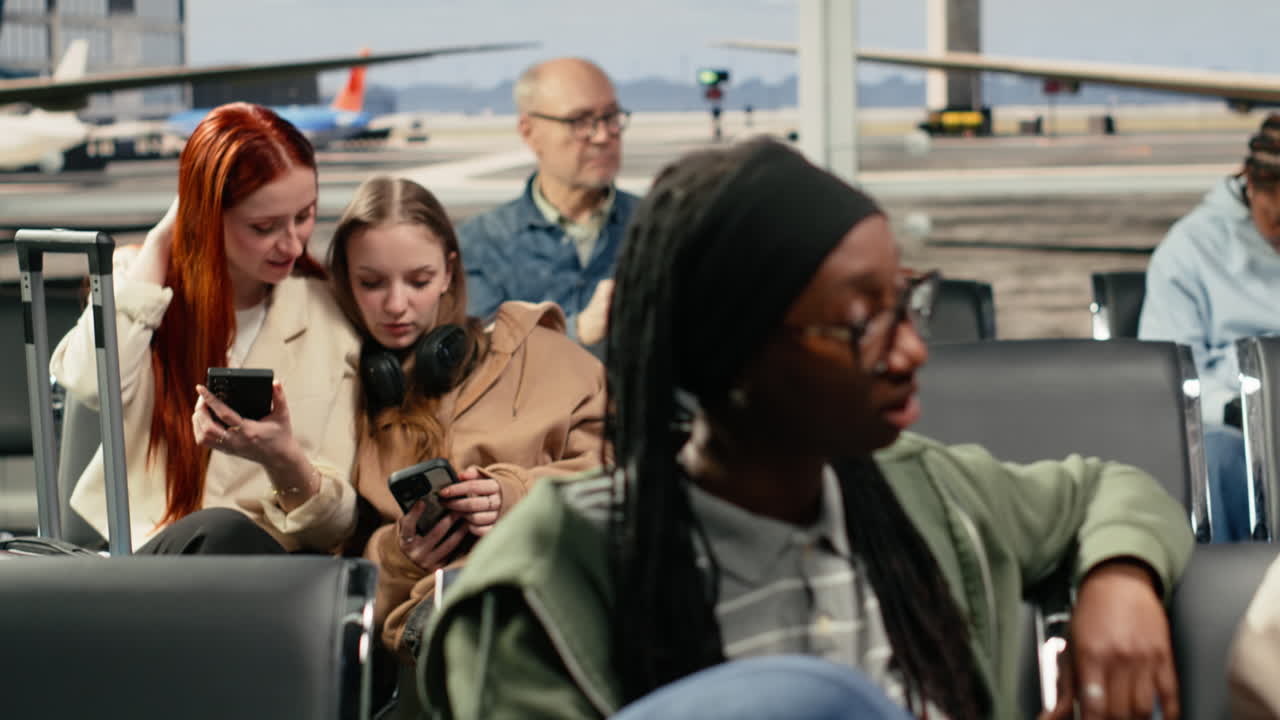 Frau und Freundin besprechen am Flughafen den Flugplan, während sie auf Stühlen sitzen