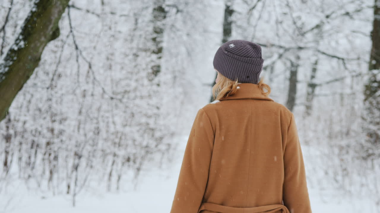 따뜻한 클래식 코트를 입은 여자가 겨울 숲을 걷는다