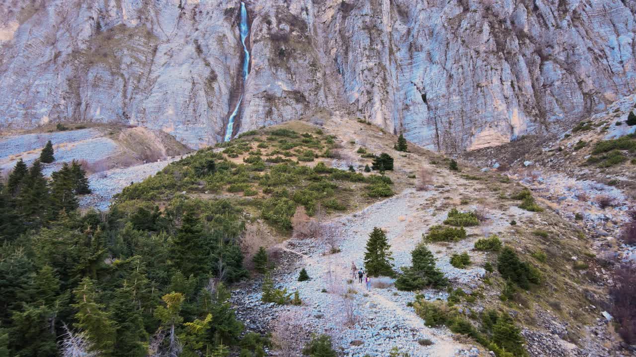 백그라운드에서 폭포에 접근하는 산을 하이킹하는 세 명의 젊은이 뒤에 공중보기