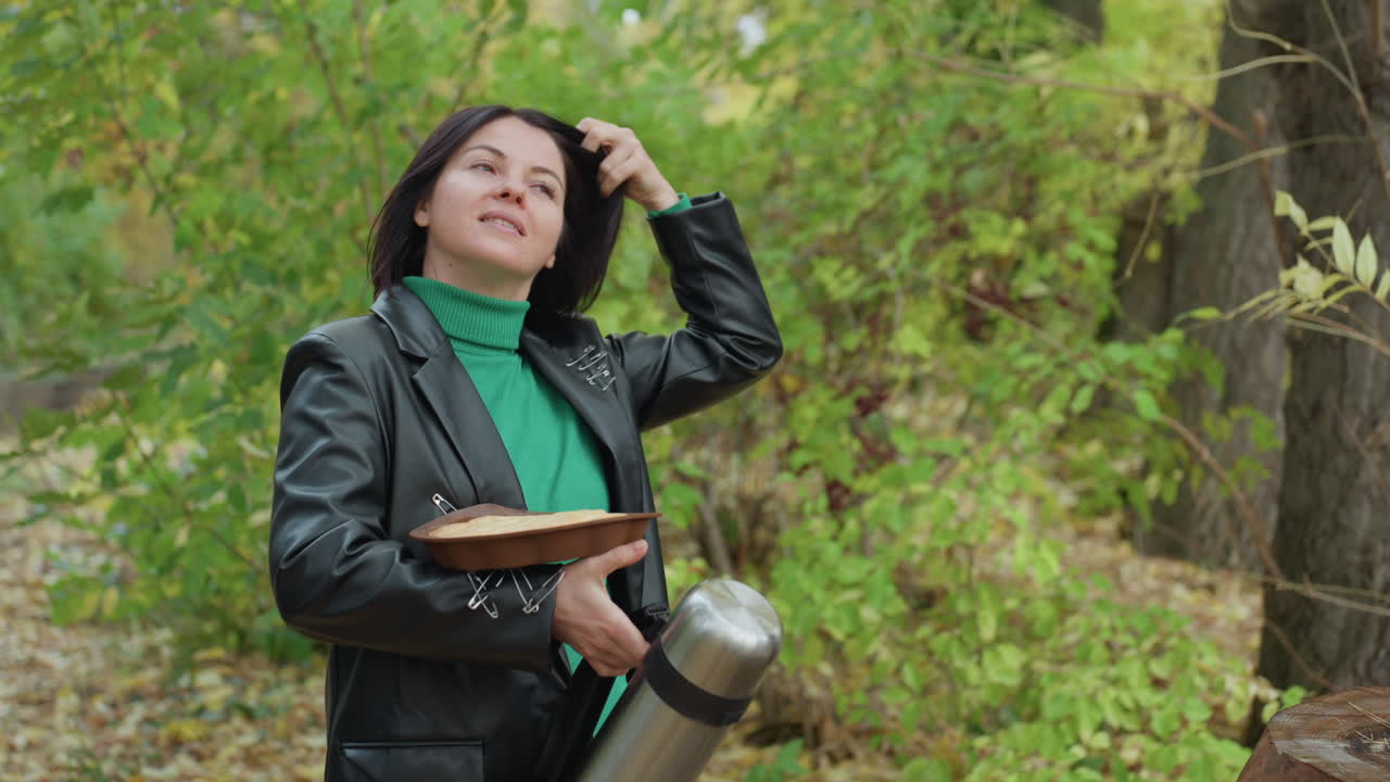 Donna di colore con giacca di pelle suona il tamburello accanto a un thermos in una foresta rigogliosa, gesti espressivi, atmosfera indie rock decisa, dolcevita verde, ritratto spontaneo, luce naturale, atmosfera autunnale
