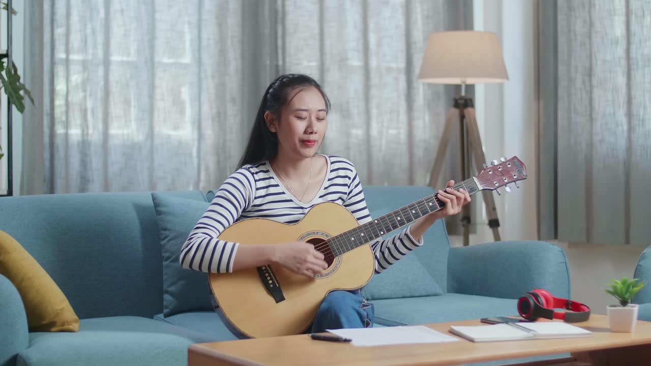 여성이 집에서 노래하고 어쿠스틱 기타를 연주하고 있습니다.