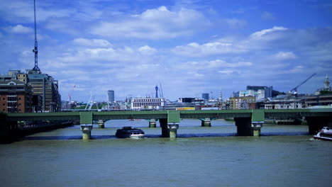 view from london bridge, ferry slowly passes under adjacent railway bridge on a sunny day