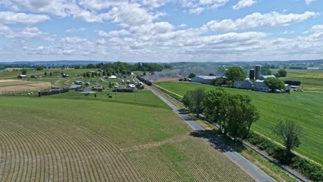 A-Drone-View-of-a-Steam-Locomotive-With-Passenger-Coaches-Approaching-over-Countryside-on-a-Beautiful-Summer-Day