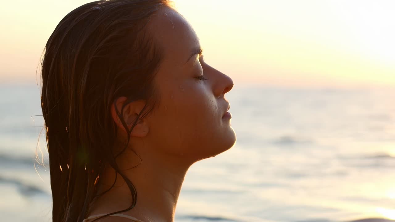 Close-up side profile of a woman by the sea at sunset, capturing a serene moment on video
