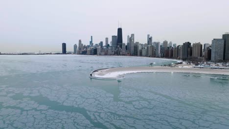 vista aérea sobre el lago helado michigan, acercándose a la playa de la avenida norte y al horizonte de la invernal chicago, estados unidos