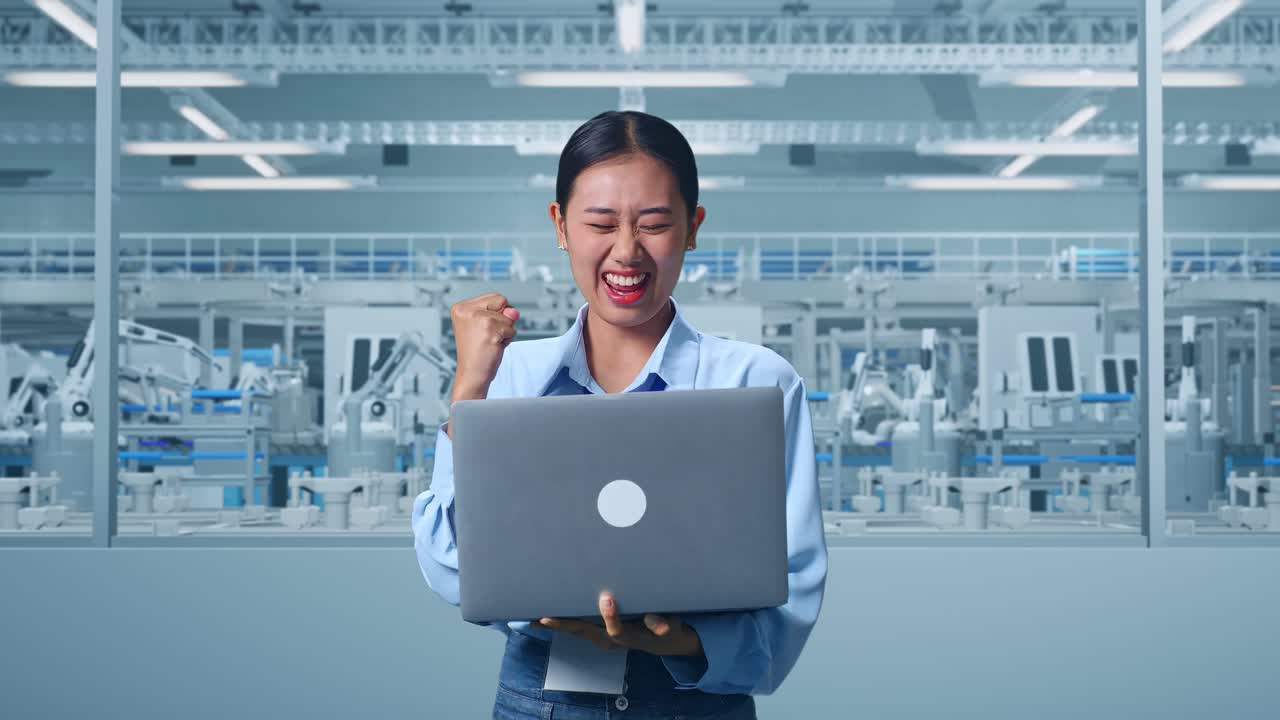 Asian Female Professional Worker Standing With Her Laptop at Factory Digitalization for Innovative Project, She Raises Her Fist Up With Screaming Goal