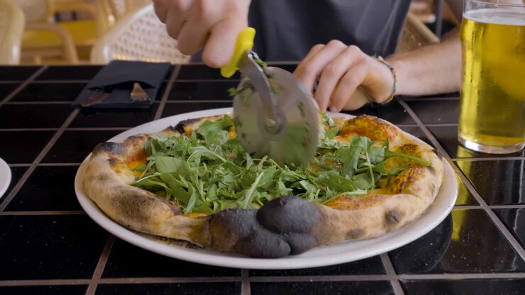 Vista frontale della mano di un commensale che taglia la pizza a un tavolo del ristorante