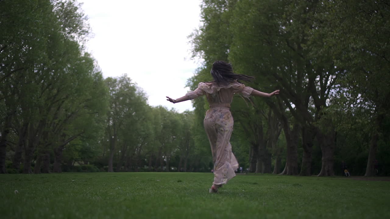 Donna latina bruna attraente e spensierata che gira su se stessa con un vestito floreale al parco a Londra, felice e allegra