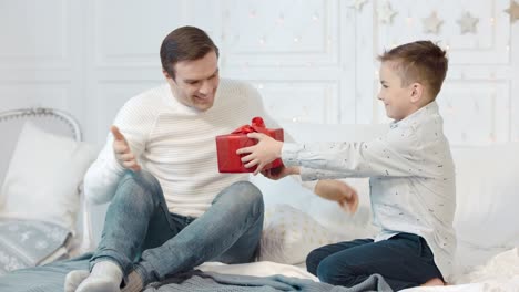 Überraschter-Vater,-Der-Im-Schlafzimmer-Ein-Neujahrsgeschenk-Bekommt.-Glücklicher-Sohn,-Der-Geschenk-überreicht