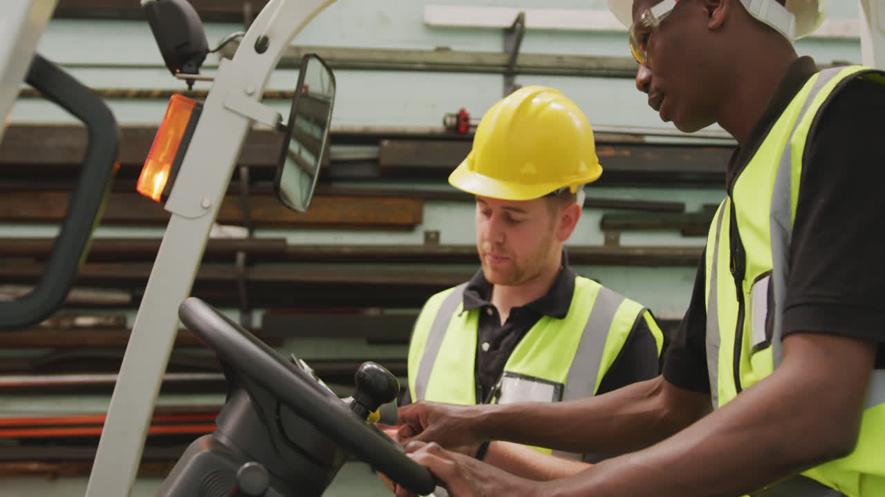 An African American and a Caucasian male factory worker at a factory talking in a warehouse area