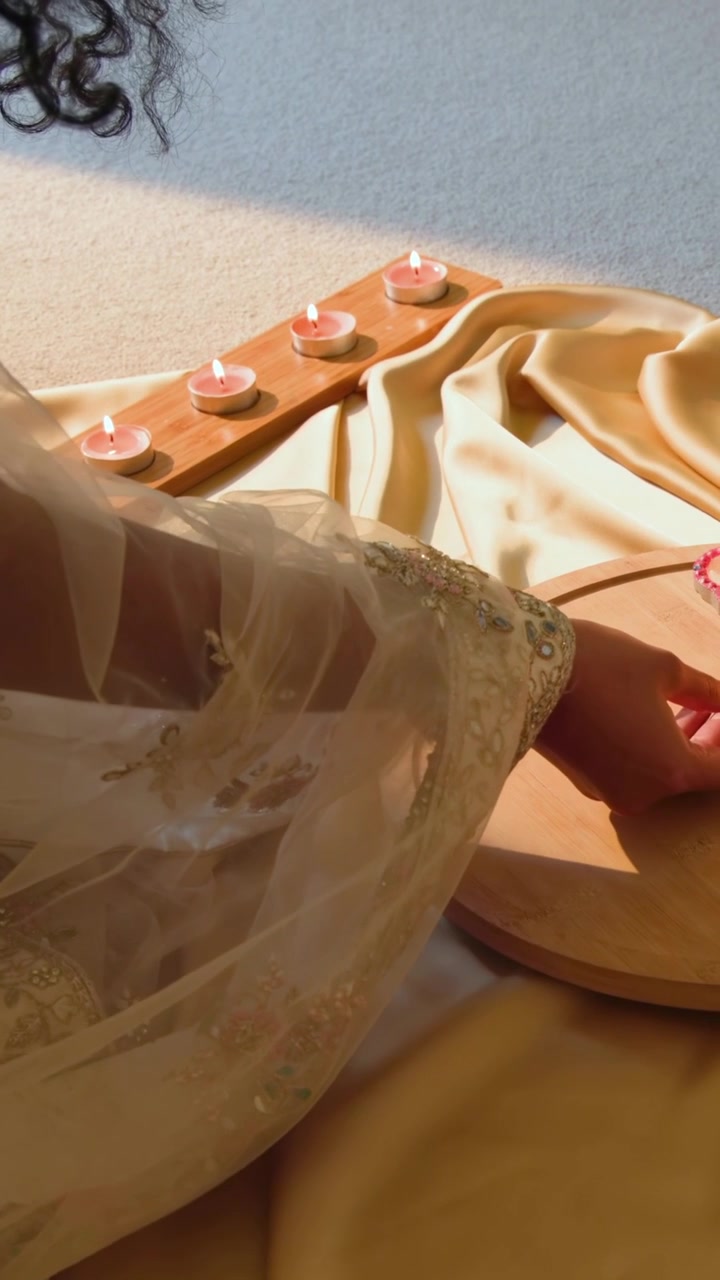 Video verticale: Donna in sari dorato che si allunga per posizionare lumini decorativi a casa, con un supporto in legno