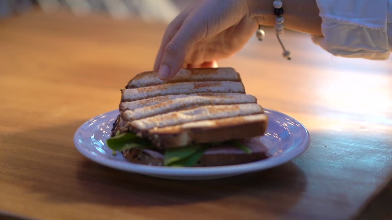Woman picking up half sandwich in slow motion back light sunset restaurant