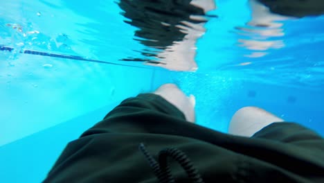 bajo el agua las piernas del hombre dentro de una piscina al aire libre con paredes de mosaico azul