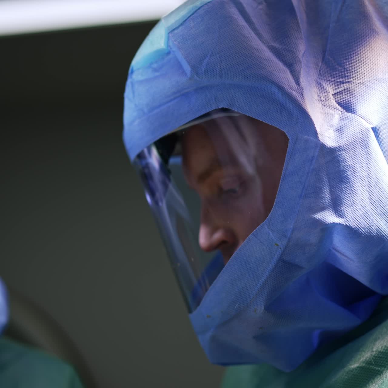 Doctor in protective helmet looks attentively at the operated area. Portrait of a surgeon during work
