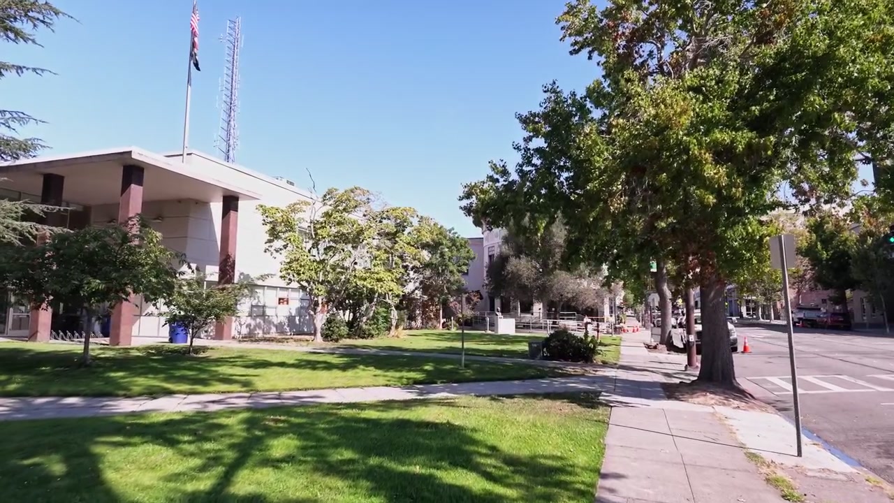 Vista in una giornata di sole del Tribunale e dell'Edificio di Pubblica Sicurezza Ronald T. Tsukamoto, sede del Dipartimento di Polizia e della prigione di Berkeley, con un prato erboso, alberi e la strada con auto di passaggio.