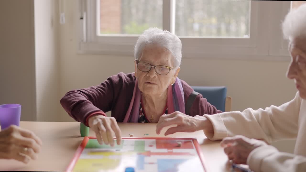 Three old friends playing board game in a nursing home