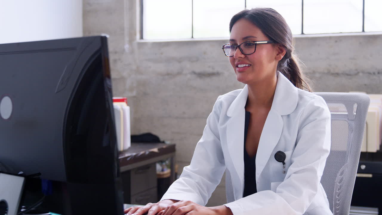 una doctora sonriente con gafas usando una computadora en la oficina