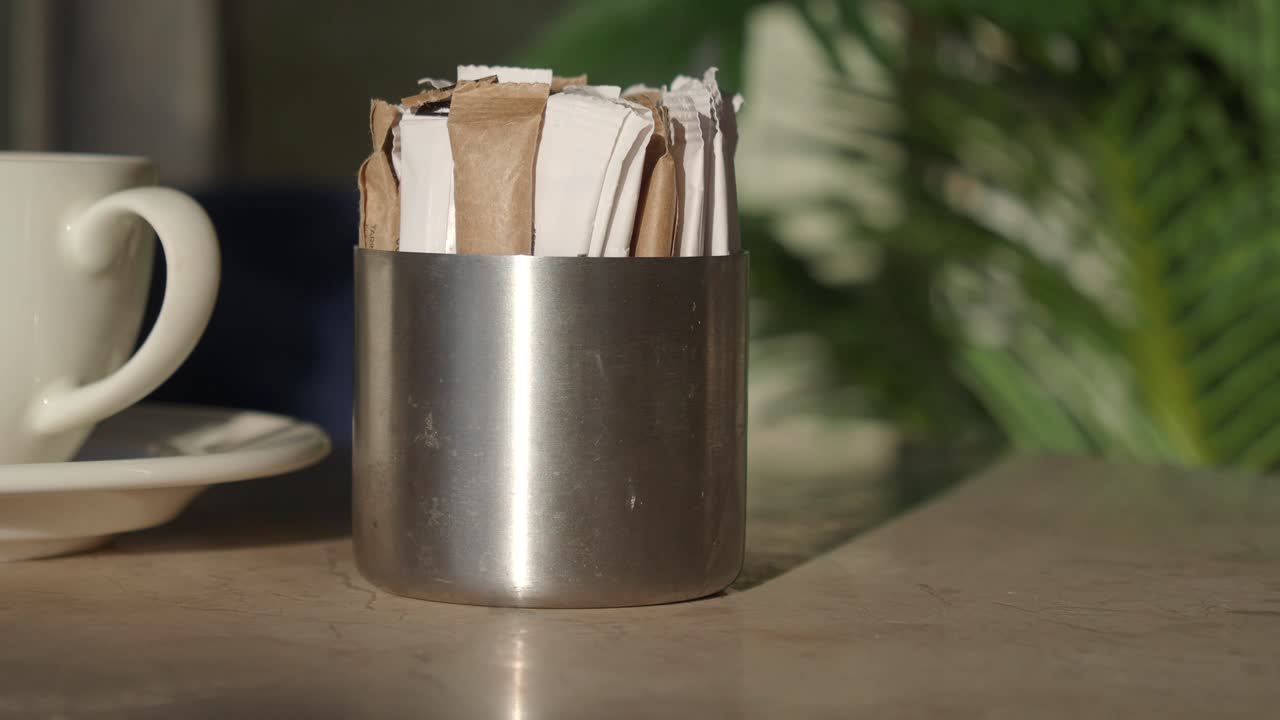 Edulcorantes en un recipiente metálico sobre una mesa de cafetería