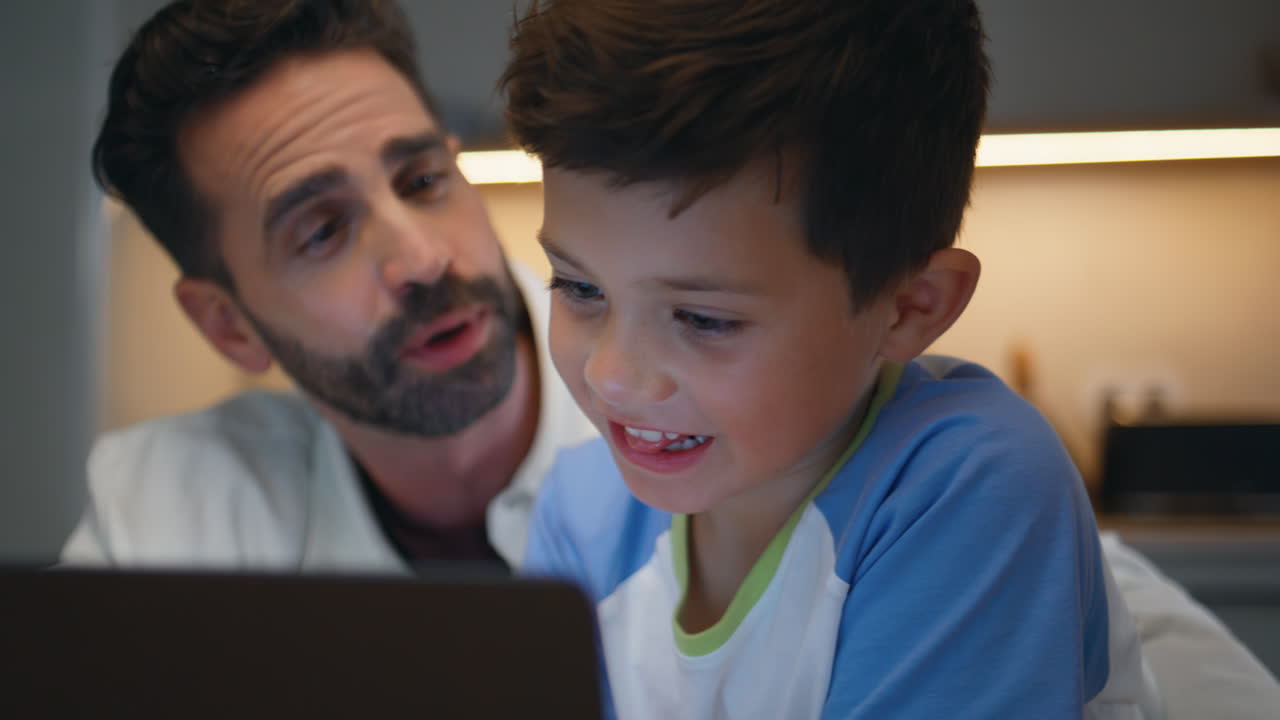 Boy man watching laptop evening apartment closeup. Father son staring computer