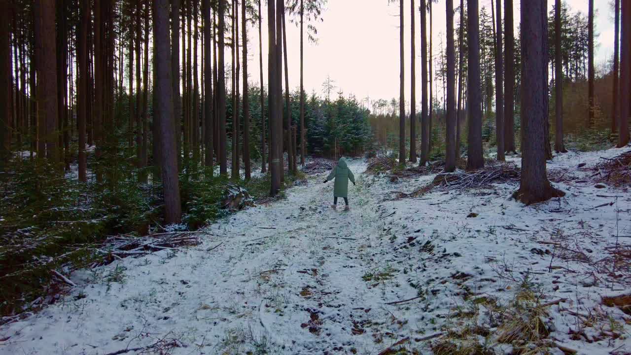 Una giovane ragazza, che si gode la stagione invernale con una giacca calda, gira su se stessa in mezzo alla foresta