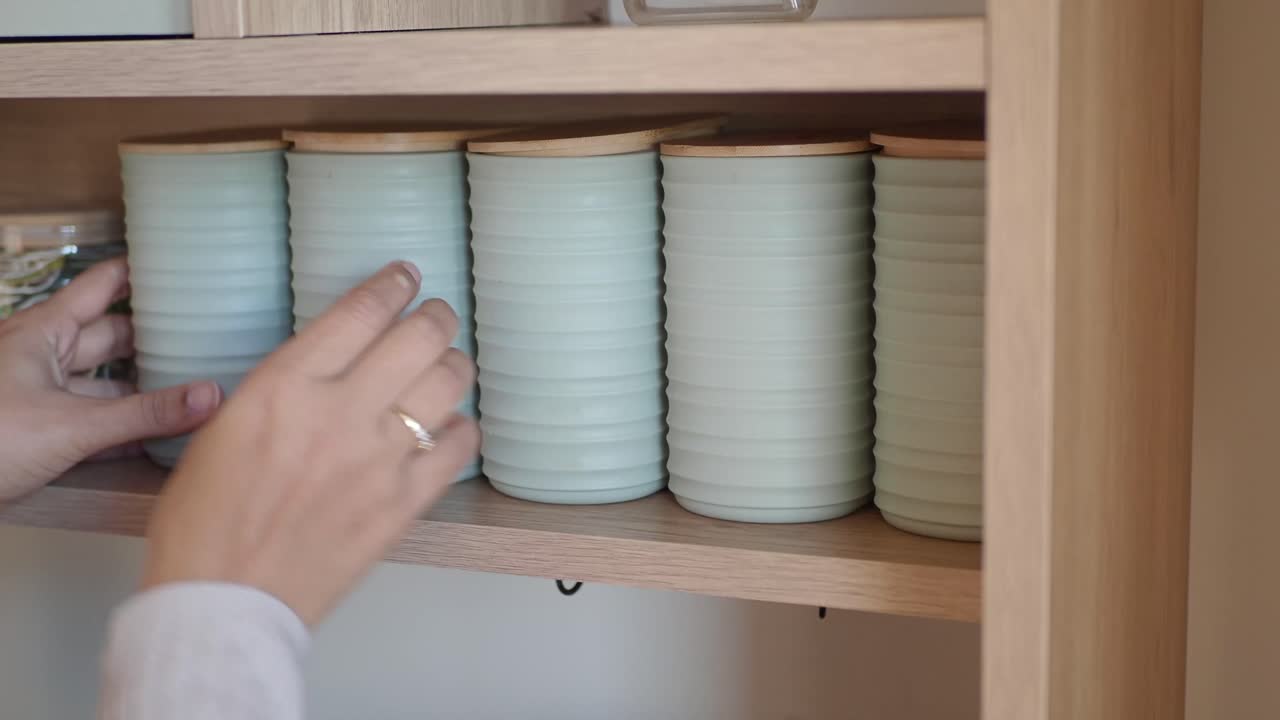 Mani che sistemano barattoli verde chiaro su uno scaffale della cucina