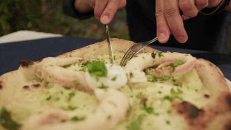 man cutting a slice of pizza with octopus with fork and knife