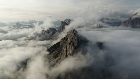 Drone-shot-circling-a-rocky-peak-covered-in-fog,-moody-day-in-Dolomites,-Italy