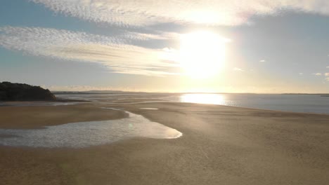 Low-flying-aerial-shot-to-rising-up-of-the-sunrise-over-sand-and-water-at-Andersons-inlet-in-Victoria-Australia